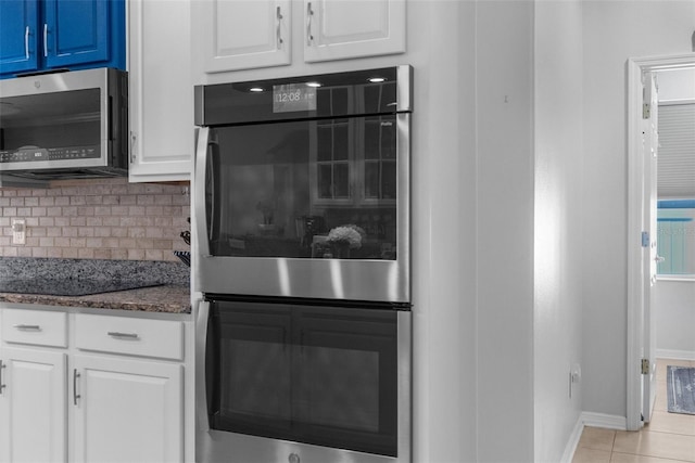 kitchen featuring stainless steel appliances, dark stone counters, white cabinets, and backsplash