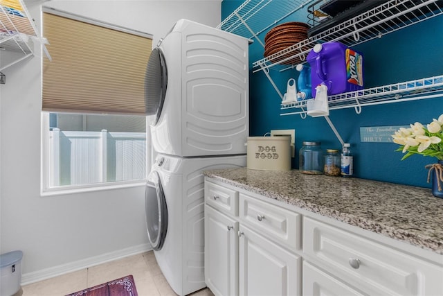 washroom with stacked washer and clothes dryer, cabinet space, baseboards, and light tile patterned floors