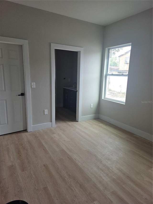 unfurnished bedroom featuring baseboards, light wood-type flooring, and connected bathroom