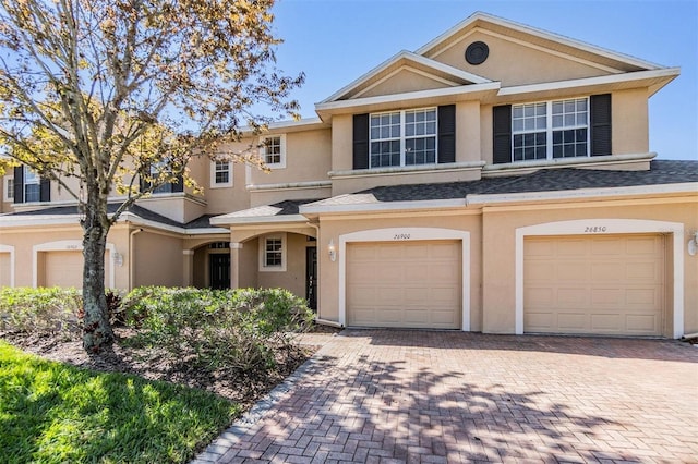 townhome / multi-family property with driveway, an attached garage, roof with shingles, and stucco siding