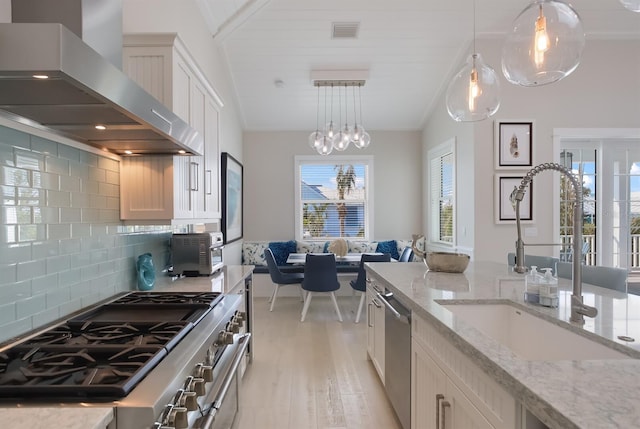 kitchen with stainless steel appliances, visible vents, light wood-style flooring, a sink, and wall chimney range hood