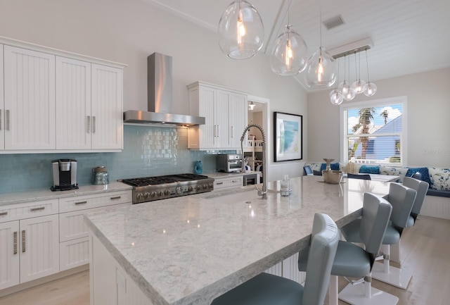 kitchen with tasteful backsplash, visible vents, stove, a kitchen island with sink, and wall chimney range hood