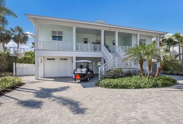 coastal home with stairway, an attached garage, covered porch, fence, and decorative driveway