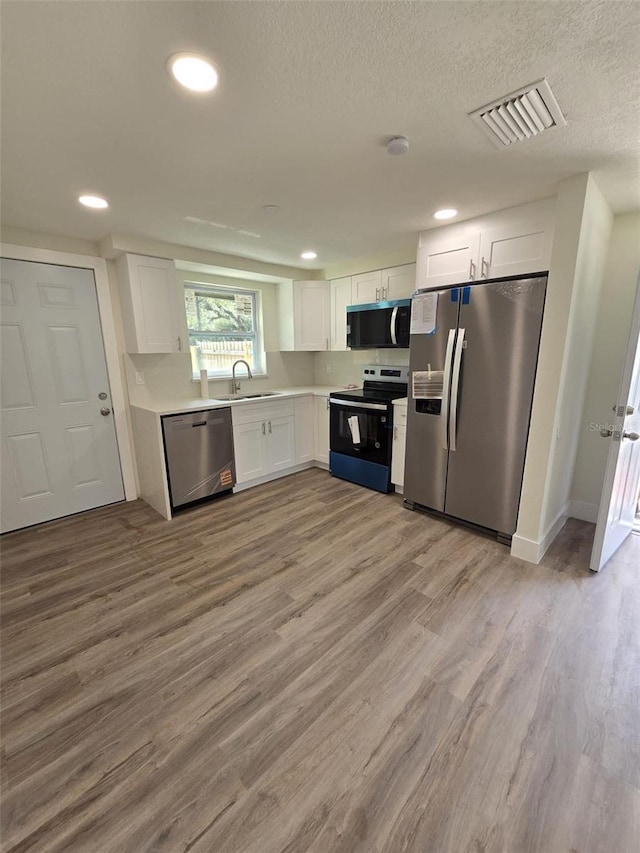 kitchen featuring visible vents, white cabinets, appliances with stainless steel finishes, light wood-style floors, and a sink