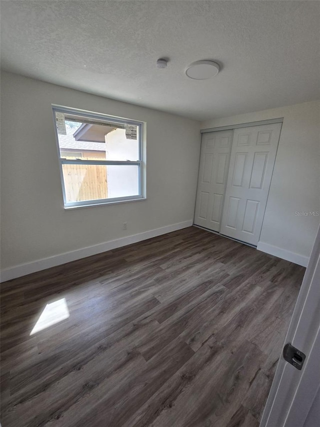 unfurnished bedroom with a closet, dark wood finished floors, a textured ceiling, and baseboards