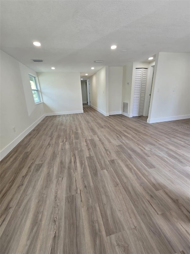 spare room with a textured ceiling, wood finished floors, visible vents, and baseboards