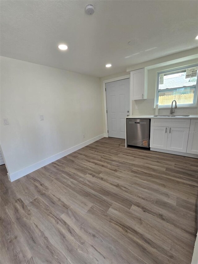 kitchen featuring baseboards, white cabinets, wood finished floors, a sink, and stainless steel dishwasher