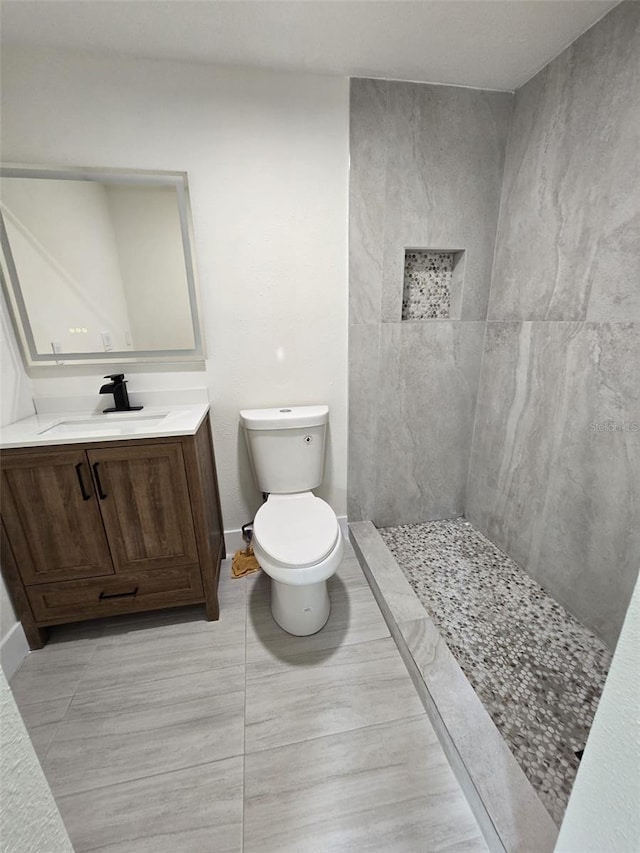 full bath featuring baseboards, a tile shower, vanity, and toilet