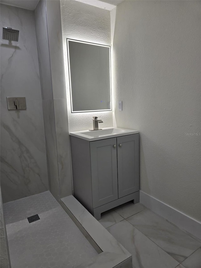 full bathroom featuring marble finish floor, a textured wall, vanity, and walk in shower