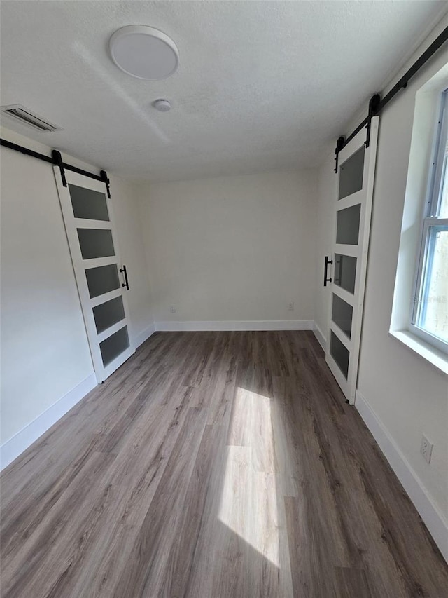 empty room with a barn door, baseboards, visible vents, wood finished floors, and a textured ceiling