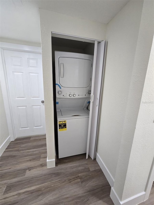 laundry room featuring dark wood-type flooring, stacked washer / dryer, and baseboards