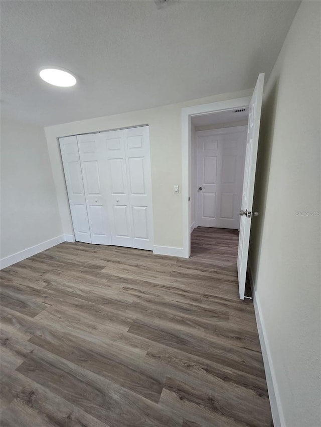 unfurnished bedroom featuring dark wood-type flooring, a closet, and baseboards