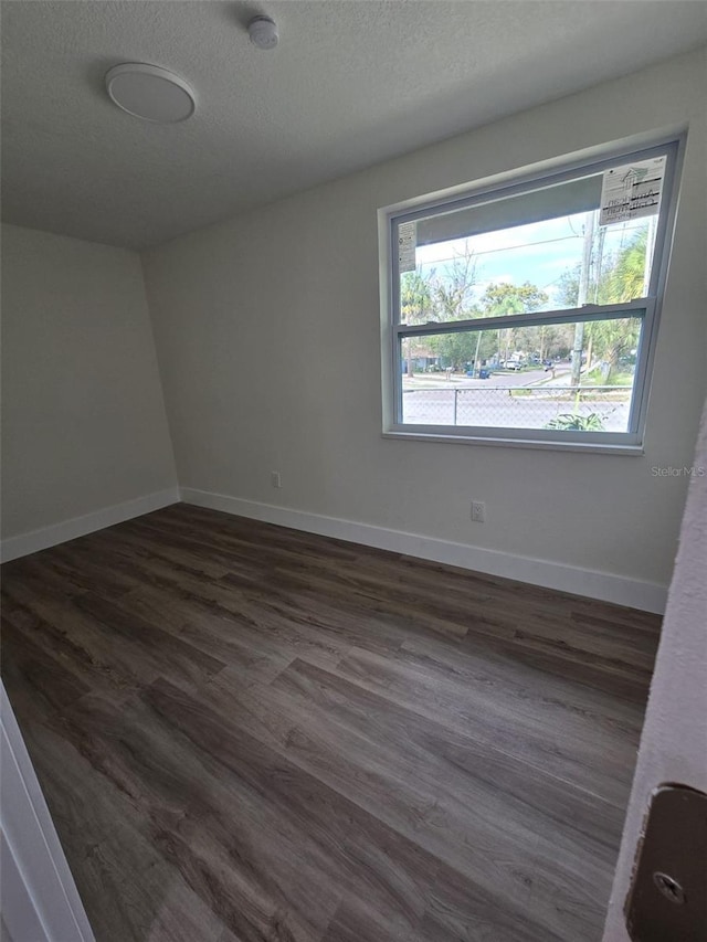 empty room featuring dark wood-style flooring, a textured ceiling, and baseboards