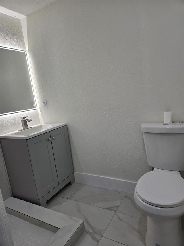 bathroom with baseboards, a textured wall, toilet, marble finish floor, and vanity