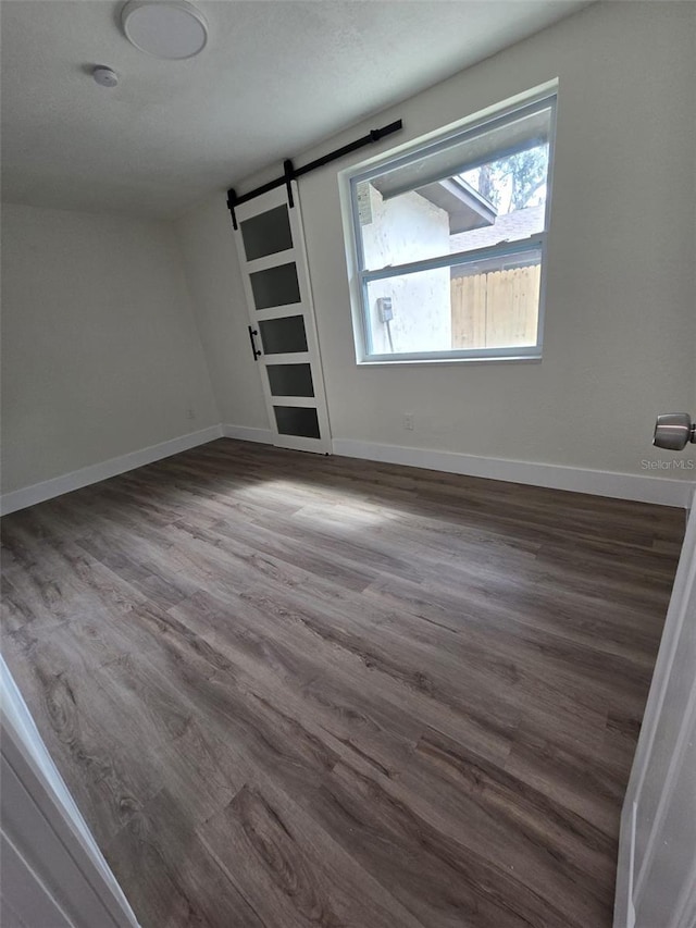 spare room featuring a barn door, baseboards, and dark wood-style flooring