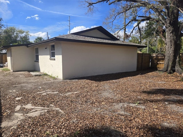 view of side of home featuring a shingled roof, fence, and stucco siding