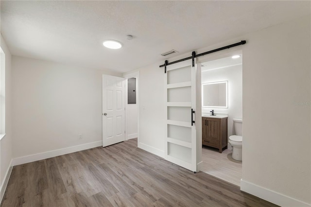 8319 N 14th St, Tampa, FL 33604 - unfurnished bedroom with a barn door, wood finished floors, baseboards, electric panel, and ensuite bath