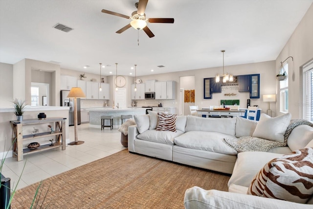 living area featuring a wealth of natural light, light tile patterned flooring, visible vents, and ceiling fan with notable chandelier