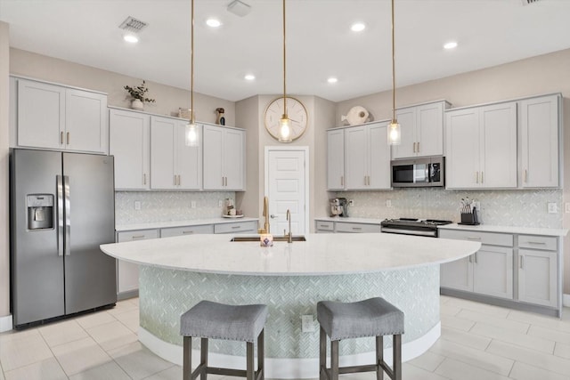 kitchen with stainless steel appliances, light countertops, visible vents, an island with sink, and a kitchen breakfast bar