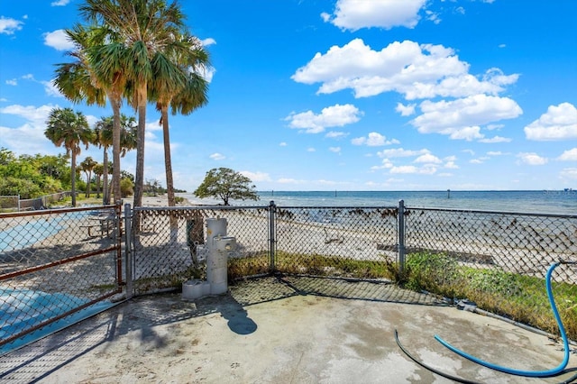 view of patio with a beach view, a water view, fence, and a gate