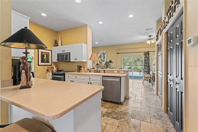 kitchen with stone tile floors, recessed lighting, appliances with stainless steel finishes, a peninsula, and white cabinetry