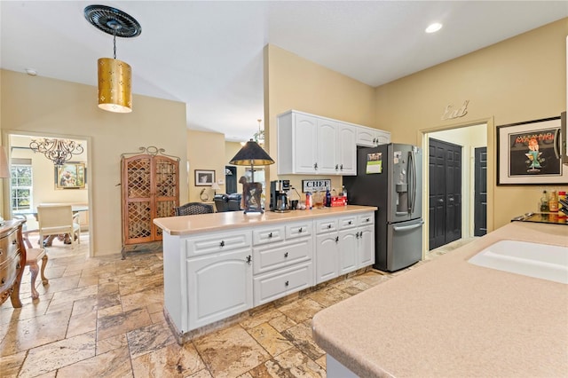 kitchen with stone tile floors, a peninsula, white cabinetry, decorative light fixtures, and stainless steel fridge