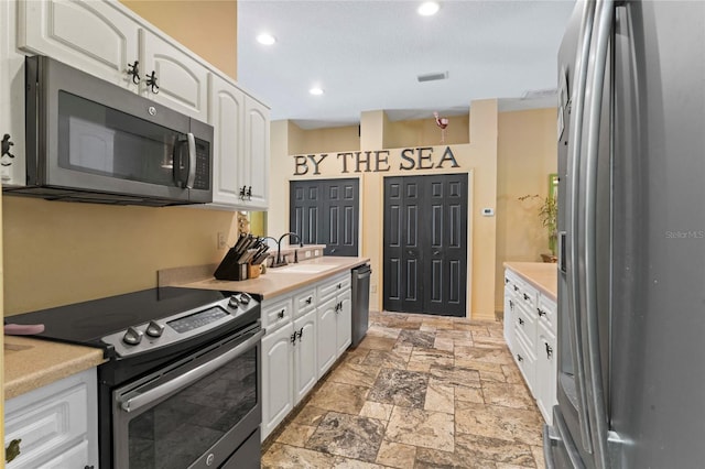 kitchen with stone tile flooring, appliances with stainless steel finishes, white cabinetry, and a sink