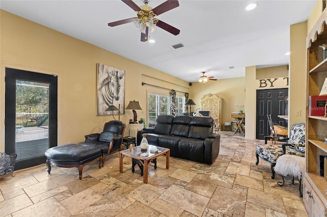 living area with stone tile floors, visible vents, and ceiling fan