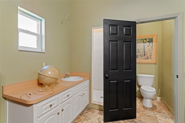 bathroom featuring vanity, stone tile floors, toilet, and baseboards