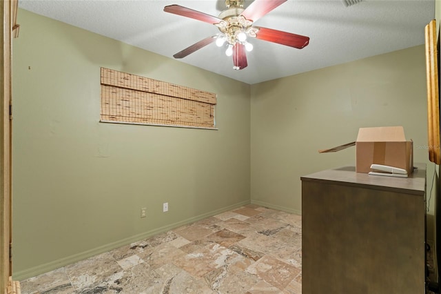 empty room with stone finish floor, a ceiling fan, baseboards, and a textured ceiling