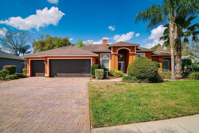 prairie-style house with an attached garage, decorative driveway, stucco siding, a chimney, and a front yard