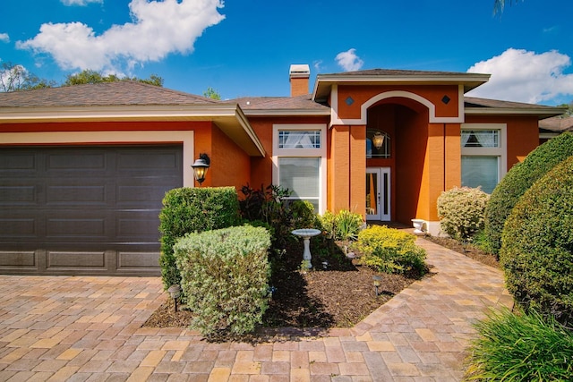 view of front of home featuring french doors, a chimney, an attached garage, and stucco siding