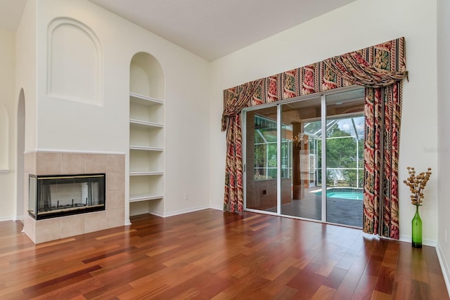 unfurnished living room with built in features, baseboards, a tiled fireplace, and wood finished floors