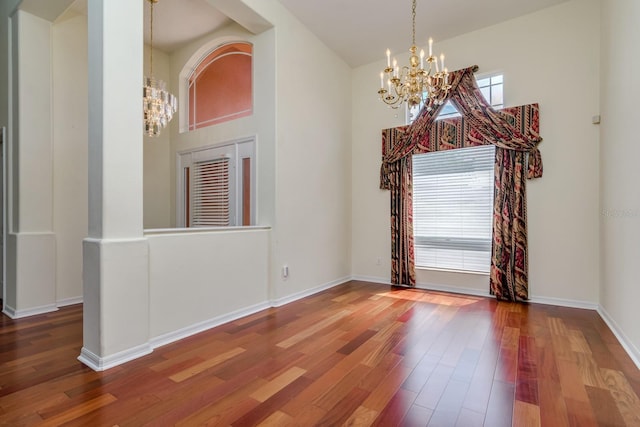 unfurnished room featuring baseboards, wood finished floors, and a notable chandelier