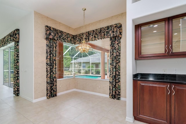 unfurnished dining area featuring baseboards, light tile patterned floors, and a notable chandelier