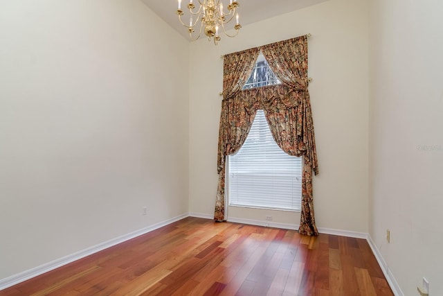 spare room with baseboards, wood finished floors, and a notable chandelier