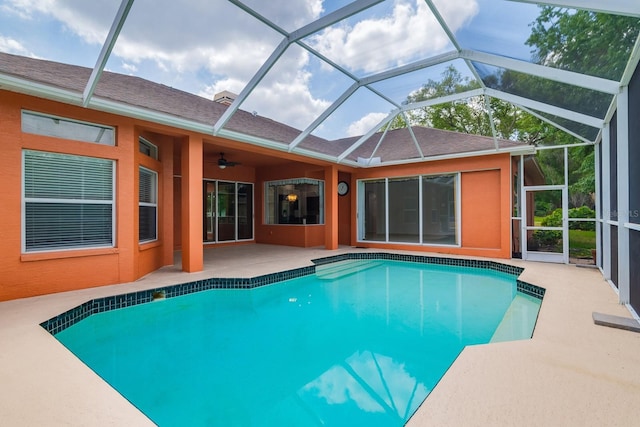 outdoor pool featuring glass enclosure, a patio, and a ceiling fan