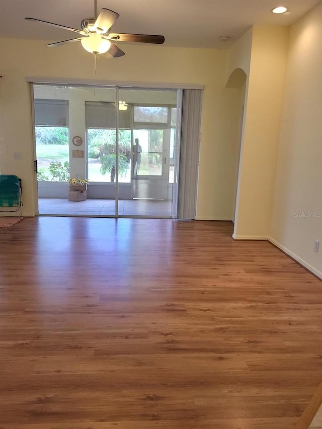 empty room featuring arched walkways, recessed lighting, a ceiling fan, wood finished floors, and baseboards