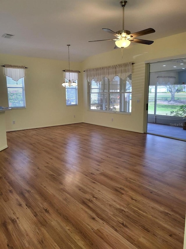 unfurnished dining area with ceiling fan with notable chandelier, visible vents, plenty of natural light, and wood finished floors