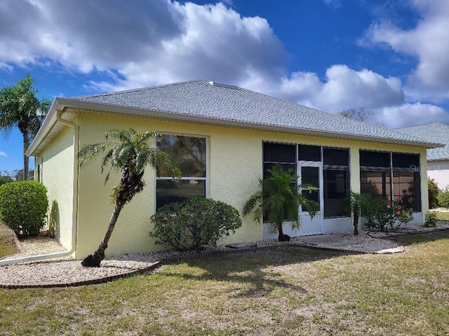 back of property with a lawn, a sunroom, and stucco siding