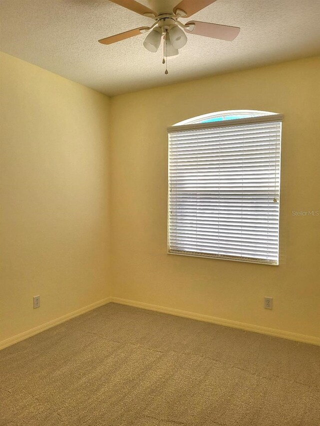 carpeted empty room featuring a textured ceiling, a ceiling fan, and baseboards