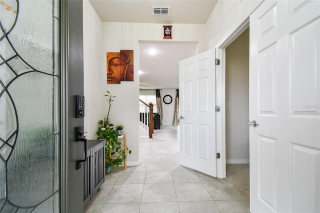 hall with light tile patterned floors, visible vents, stairway, and baseboards