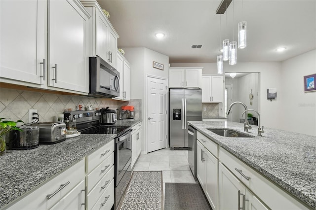 kitchen with appliances with stainless steel finishes, dark stone countertops, a sink, and visible vents