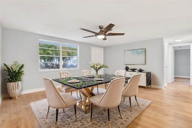 dining room with light wood finished floors, a ceiling fan, and baseboards