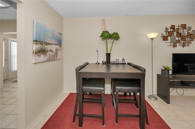 tiled dining space featuring baseboards and a textured ceiling