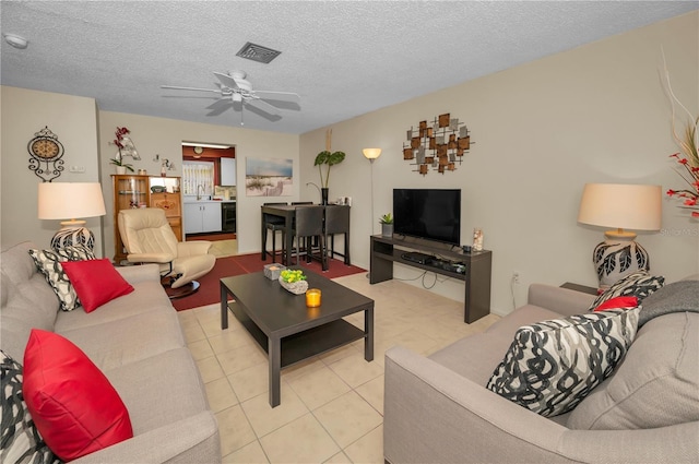 living room with a textured ceiling, visible vents, a ceiling fan, and tile patterned floors