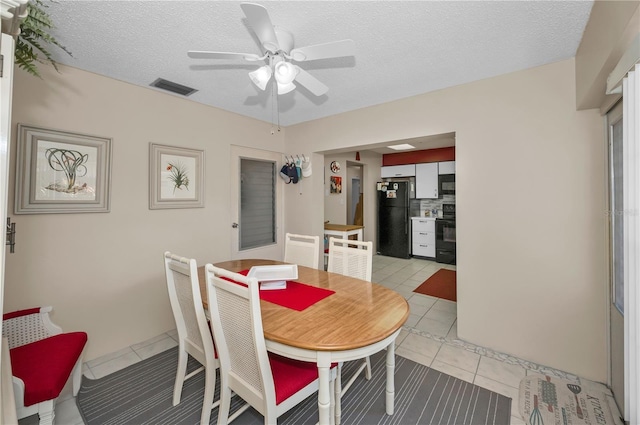 dining space with a textured ceiling, light tile patterned flooring, visible vents, and a ceiling fan