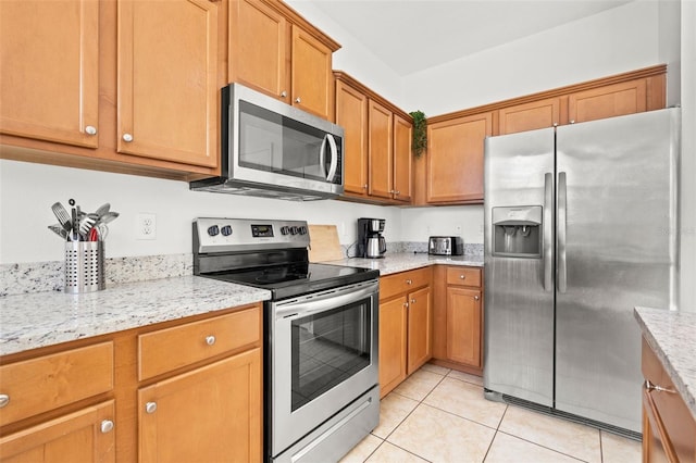 kitchen featuring light tile patterned floors, stainless steel appliances, light stone countertops, and brown cabinetry