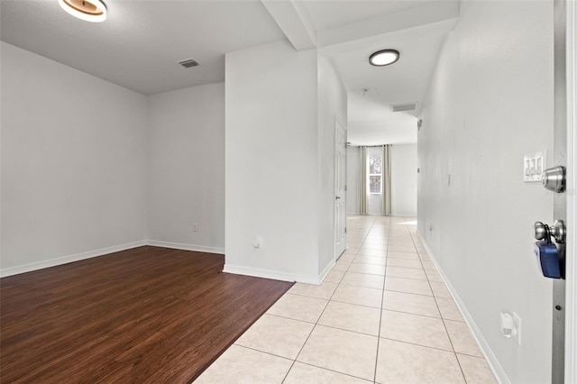 hallway featuring beam ceiling, visible vents, baseboards, and light wood-style floors