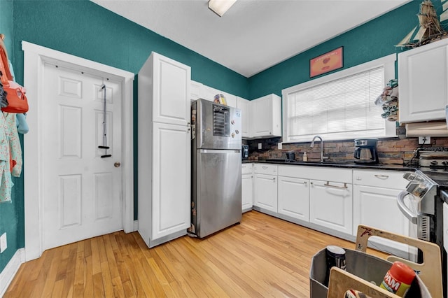 kitchen featuring stainless steel appliances, dark countertops, white cabinets, a sink, and light wood-type flooring